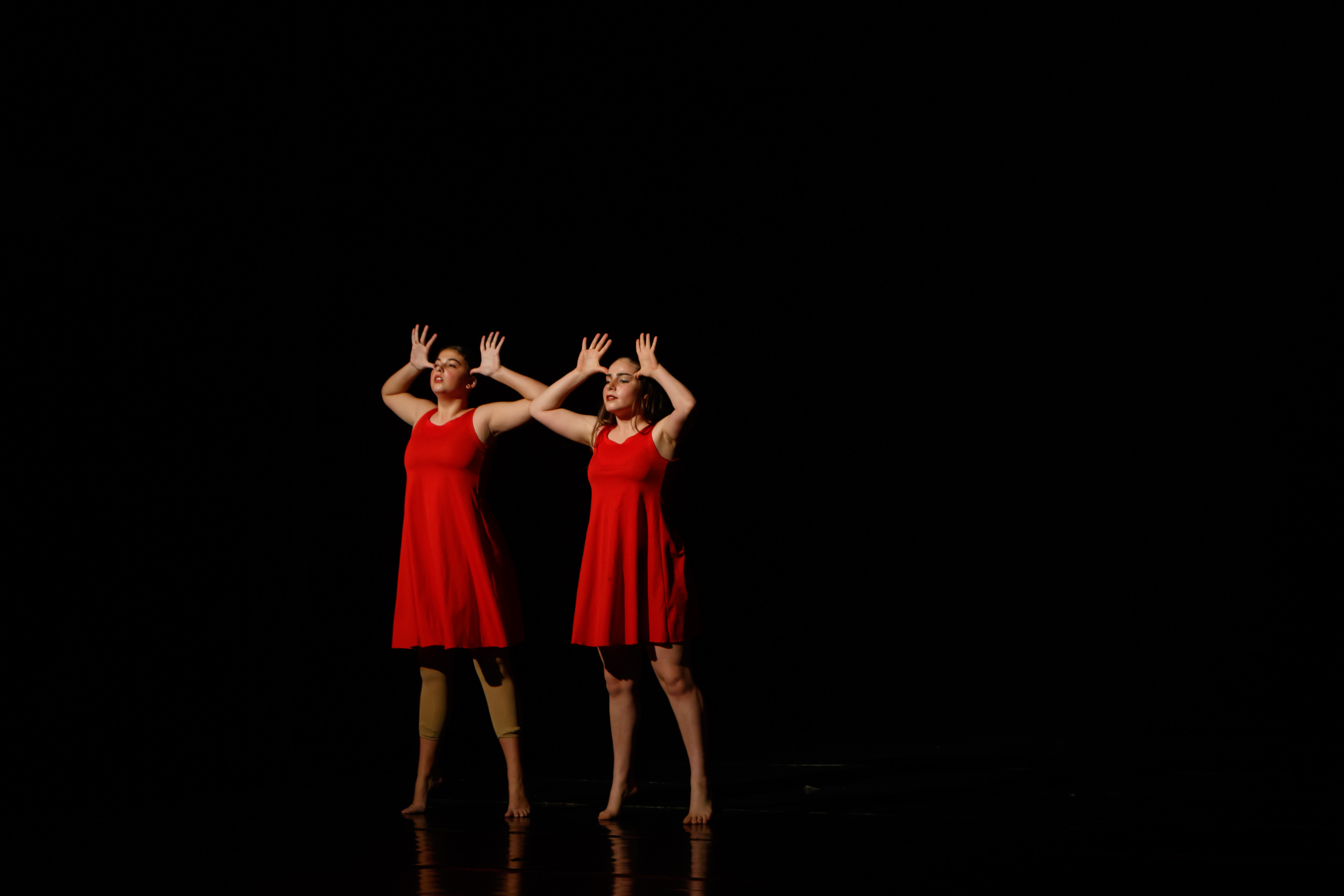 Two dancers in red dresses on a dark stage